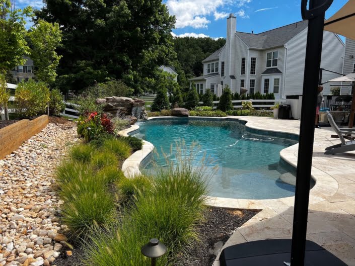 Custom freeform pool with waterfall and landscaping Outdoor living room, pergola, and pool Reisterstown MD